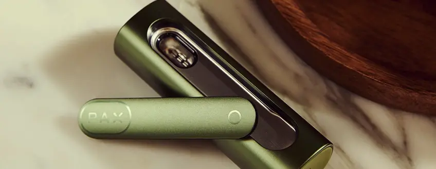 Vaporizzatore Pax Flow aperto Primo piano del vaporizzatore Pax Flow aperto che rivela la sua camera interna piena di cannabis, tenuto da una mano in un'ambientazione esterna casual con luce naturale.