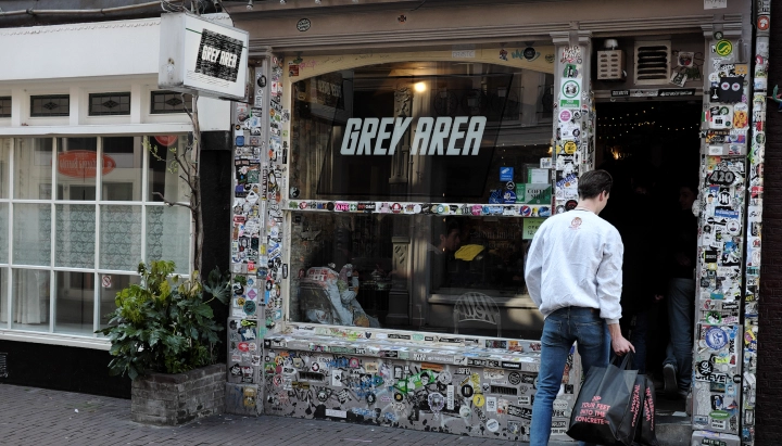 Coffeeshop di cannabis nei Paesi Bassi Ingresso di un coffeeshop di cannabis nei Paesi Bassi con insegna Grey Area e facciata ricoperta di adesivi.