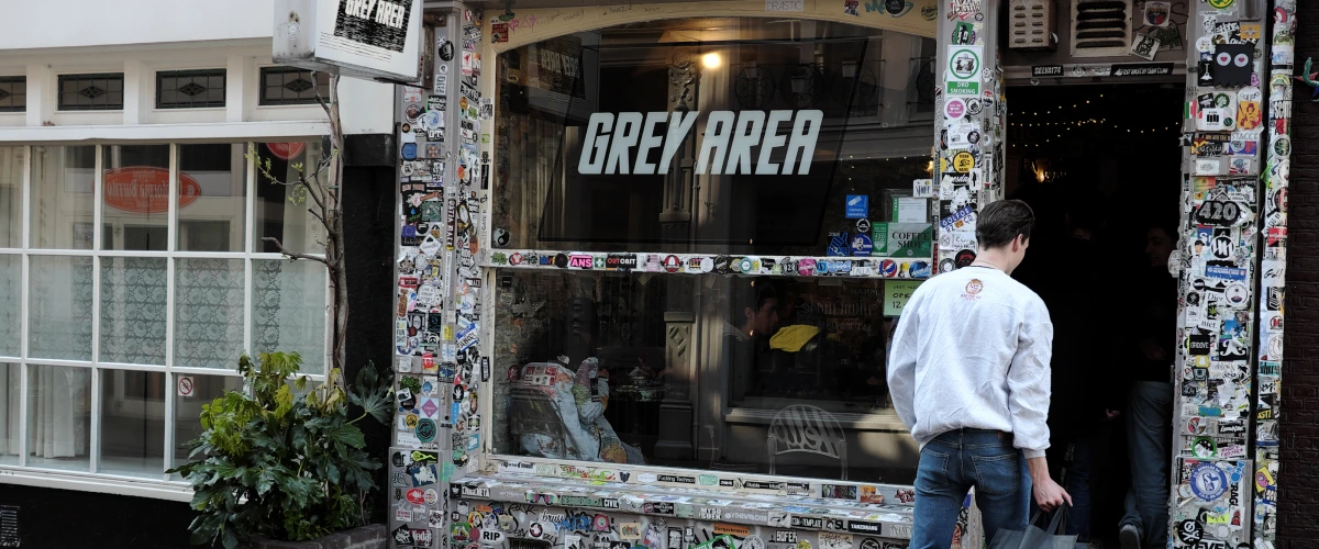 Coffeeshop di cannabis nei Paesi Bassi Ingresso di un coffeeshop di cannabis nei Paesi Bassi con insegna Grey Area e facciata ricoperta di adesivi.