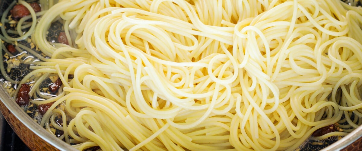 Spaghetti scolati mescolati con pancetta croccante e burro infuso in padella, quarto passo per una carbonara infusa alla cannabis