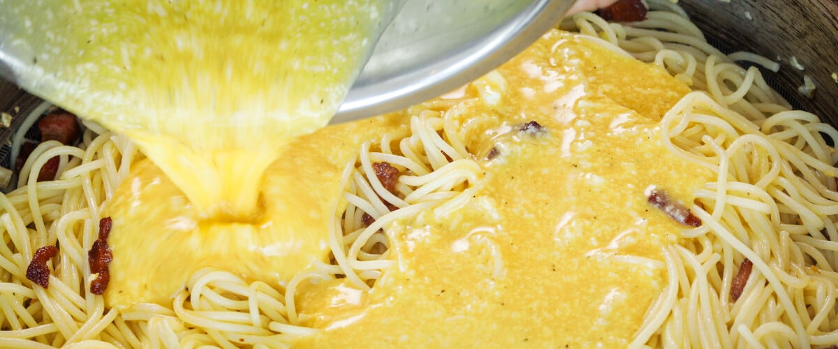 Composto di uova e formaggio versato sugli spaghetti caldi in padella, quinto passo per una carbonara infusa alla cannabis