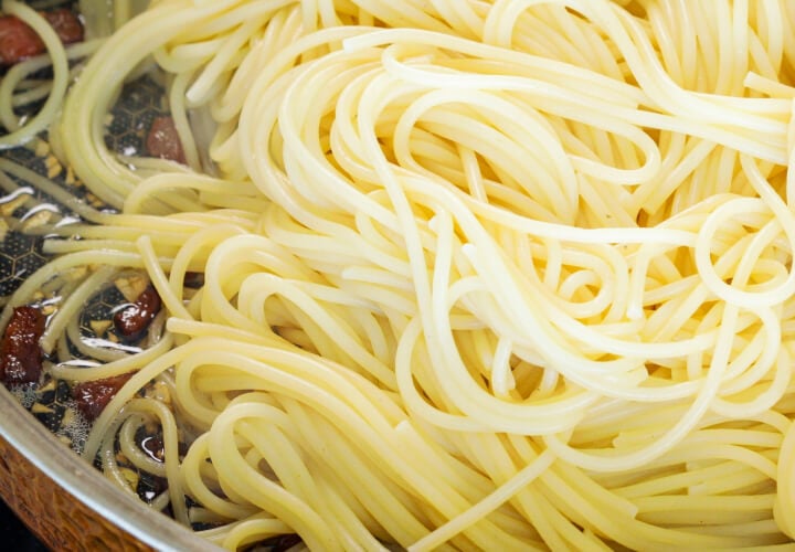 Spaghetti scolati mescolati con pancetta croccante e burro infuso in padella, quarto passo per una carbonara infusa alla cannabis