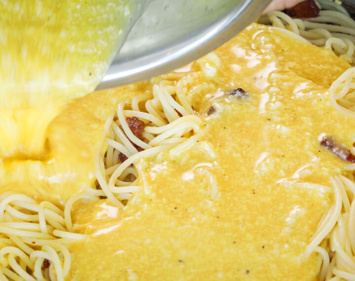 Composto di uova e formaggio versato sugli spaghetti caldi in padella, quinto passo per una carbonara infusa alla cannabis